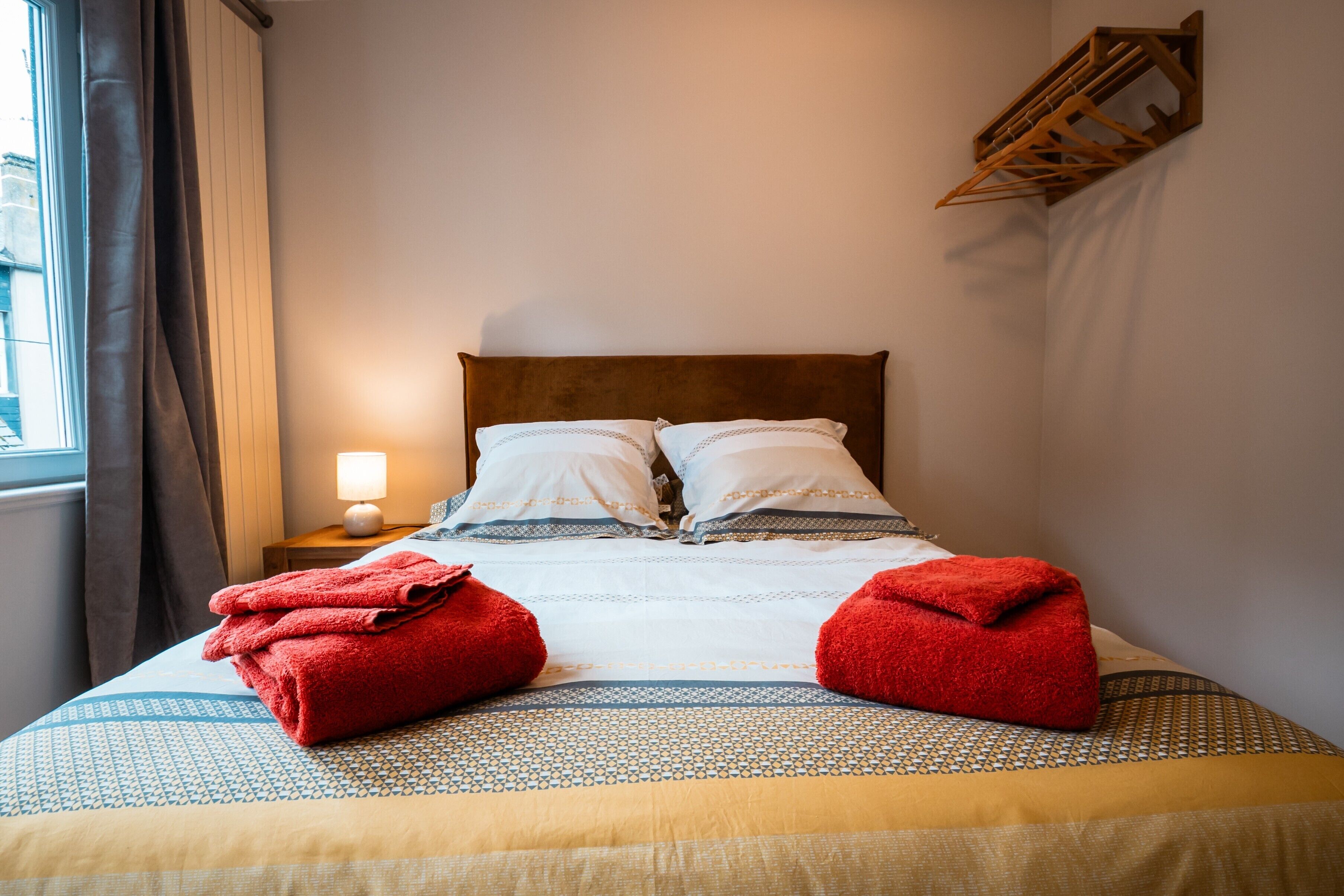 A neatly made bed with a patterned bedspread, pillows, and two red towels placed on the bed.