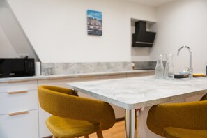 A modern kitchen with a marble countertop, two mustard-colored chairs, a black microwave, and a hanging light fixture. - Guesthouse “Murmures De La Risle” in Pont-Audemer, Normandy (Pont-Audemer)