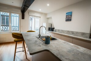 A modern kitchen with a marble countertop, a sink, a yellow chair, and a window with a view. - Guesthouse “Murmures De La Risle” in Pont-Audemer, Normandy (Pont-Audemer)