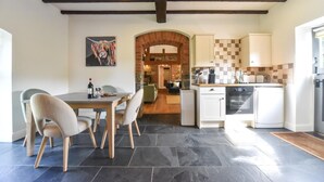 A modern kitchen with a dining area, featuring a stone floor, wooden chairs, and a view into the living room. - 2 Bed in Ashbourne (oc-dcbob) (Kniveton)