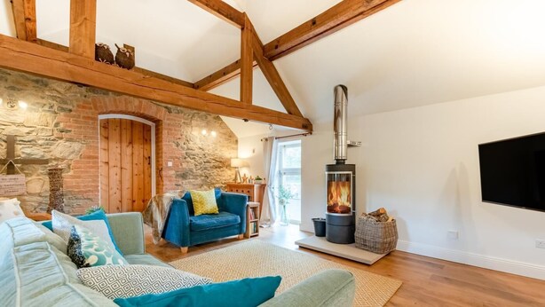 A cozy living room with exposed wooden beams, a stone wall, a blue sofa, a fireplace, and a flat-screen TV. - 2 Bed in Ashbourne (oc-dcbob) (Kniveton)