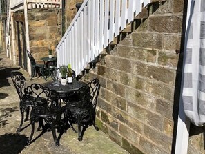 A stone wall with a white fence, a round table with chairs, and a bottle of wine. - 2 Bed in Whitby (oc-w050) (Whitby)