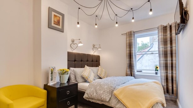 Ein Schlafzimmer mit Bett, Nachttisch, Stuhl und einem Fenster mit Vorhängen.