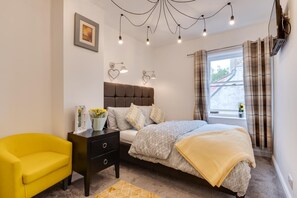 A bedroom with a bed, bedside table, chair, and a window with curtains.
