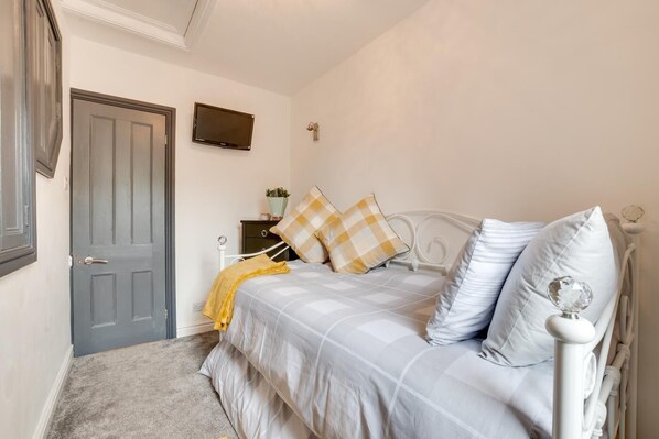 A bedroom with a bed, a bedside table, a TV, and a door.