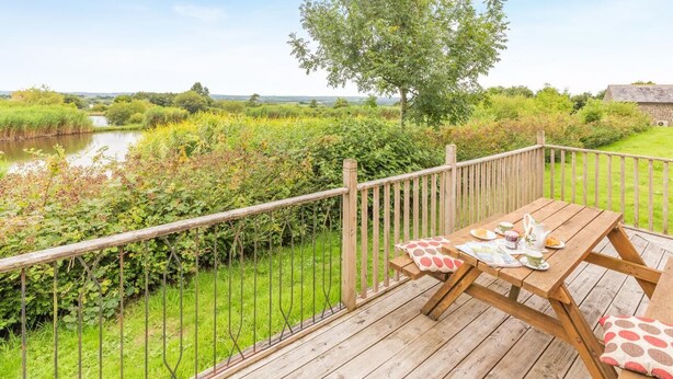 En träveranda med ett bord dukat för te, med utsikt över en flod och grönskande omgivningar.
