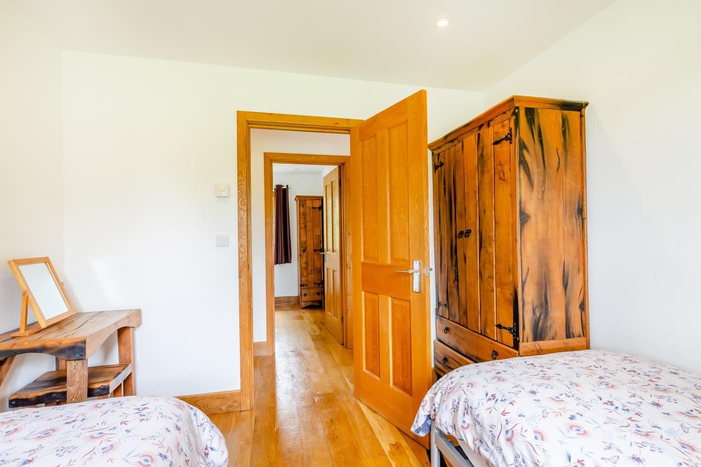 A bedroom with two beds, wooden wardrobe, and a desk with a picture frame.