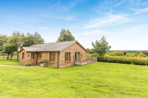 A wooden cabin with a sloped roof, a small porch, and a fenced yard. - 3 Bed in Shebbear (oc-l32583) (Shebbear)