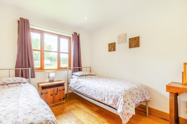 Une chambre avec deux lits simples, une commode en bois, une table de chevet et une fenêtre avec des rideaux.
