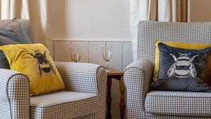 Twee geruite fauteuils met gele en zwarte bijenkussens, een tafeltje met wijnglazen en een witte muur met gordijnen.
