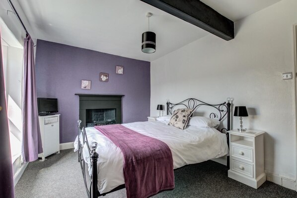 A bedroom with a bed, bedside tables, a fireplace, and a television.