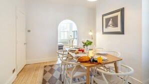 A dining area with a wooden table set for four, white chairs, a chandelier, and a framed picture on the wall. - 3 Bed in Harrogate (oc-d32616) (Harrogate)