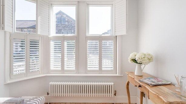 A room with a bay window, white radiator, wooden floor, and a small table with a vase of flowers. - 3 Bed in Harrogate (oc-d32616) (Harrogate)