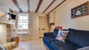 A cozy living room with a blue sofa, a patterned cushion, a stone wall, and a window with a view. - 2 Bed in Whitby (oc-w075) (Whitby)