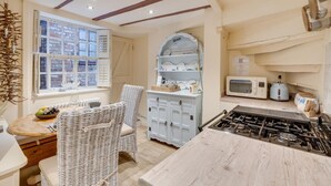 A cozy kitchen with a gas stove, white cabinets, wicker chairs, and a window with a view of buildings. - 2 Bed in Whitby (oc-w075) (Whitby)