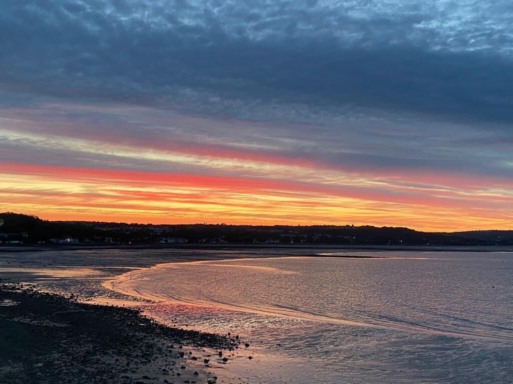 A sunset over a calm body of water with a distant shoreline.
