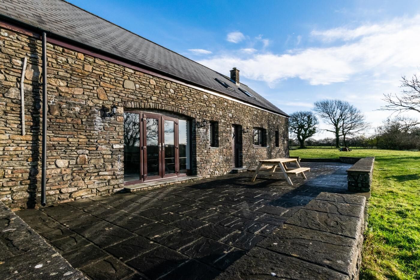 A stone building with a patio area, a wooden table, and a bench.
