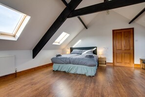 Ein Schlafzimmer mit schrägen Wänden, einem Bett, einer Holztür und einem Fenster.