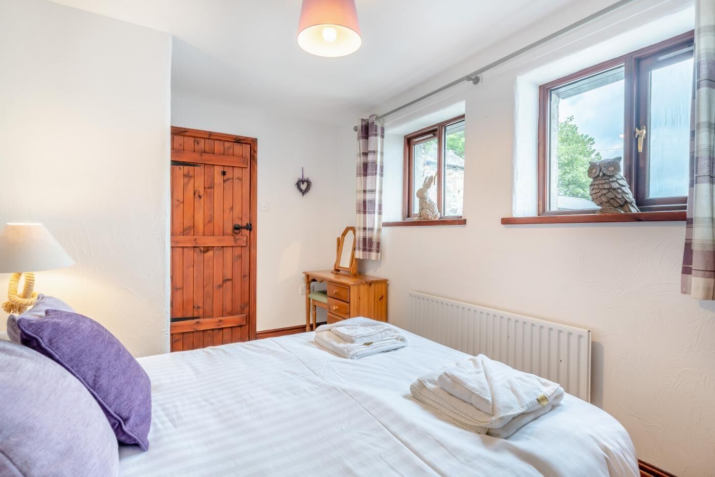 Ein Schlafzimmer mit einem Bett, einem Holzschrank, einer Kommode, einem Fenster mit Vorhängen und einer Heizung.