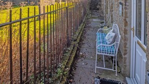 Une ruelle étroite avec une tour en pierre, une clôture en métal et un banc devant un bâtiment doté d’une porte.
