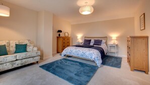 Une chambre à coucher avec un lit, une commode en bois, une table de chevet, une coiffeuse, un canapé et un tapis bleu.