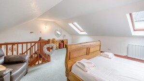 Un dormitorio con una cama de madera, un aparador de madera, un cómoda, una escalera de madera y un tragaluz.