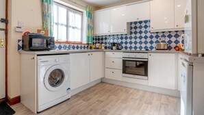 A compact kitchen with a washing machine, oven, microwave, and a tiled backsplash. - 2 Bed in Whitby (oc-w086) (Whitby)