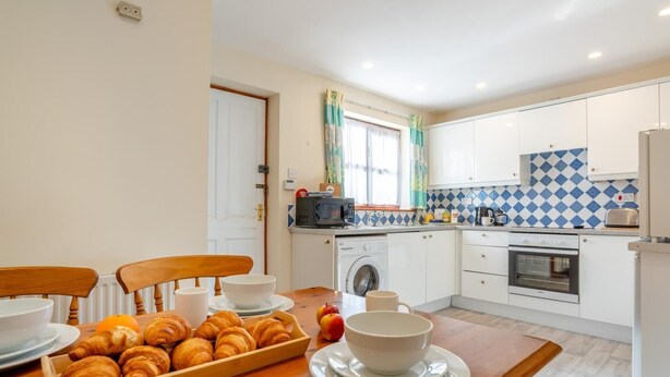 A compact kitchen with a dining table set for breakfast, including croissants and apples. - 2 Bed in Whitby (oc-w086) (Whitby)