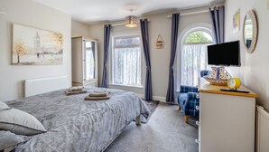Ein Schlafzimmer mit Bett, Kommode, Fernseher und einem Fenster mit Vorhängen.