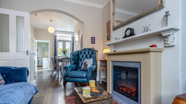 Ein Wohnzimmer mit Kamin, einem blauen Sessel und einem Essbereich im Hintergrund.
