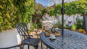 Eine Terrasse mit einem runden Metalltisch, zwei Stühlen, einer Tablett mit Kaffeekanne, Tassen und einer Schmetterlingsdeko.