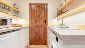 Eine Küche mit Holztür, weißen Schränken, einer Mikrowelle, einer Waschmaschine und Regalen mit Geschirr.