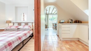 Ein Schlafzimmer mit einem Bett, einem Nachttisch und einer Lampe. Es gibt eine Küchenzeile mit einem Spülbecken, einem Herd und Schränken.
