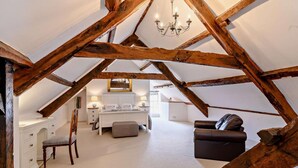 Een slaapkamer op zolder met zichtbare houten balken, een bed, een bureau en een stoel.