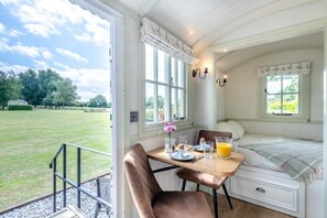 A cozy room with a bed, a dining table with chairs, and a view of a grassy field. - 1 Bed in Barsham (oc-n32504) (Barsham)