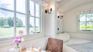 Et soveværelse med en seng, et bord med morgenmad og store vinduer med udsigt til grønne omgivelser.