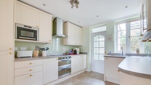 Une cuisine moderne avec des meubles blancs, un four à micro-ondes encastré, une hotte en acier inoxydable et un four double.
