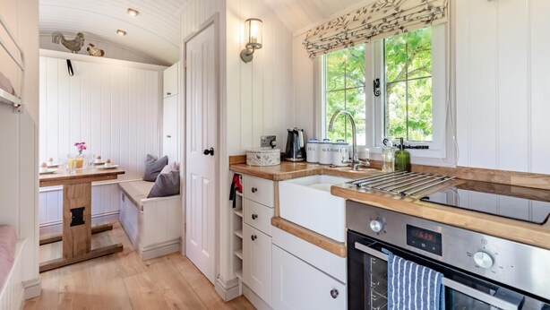 A compact kitchen with white cabinetry, a wooden countertop, a built-in oven, and a window with a view of greenery outside. - 2 Bed in Barsham (oc-s32505) (Barsham)