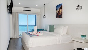 Ein modernes Hotelzimmer mit einem großen Bett, Meerblick, einem Flachbildfernseher und einem kleinen Tisch mit Taschentuchbox.