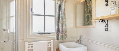 A bathroom with a window, a sink, a mirror, and a shower.