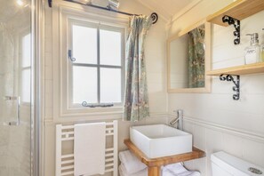 A bathroom with a window, a sink, a mirror, and a shower.