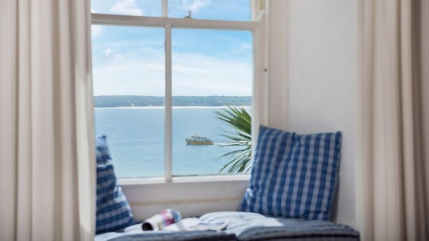A room with a view of the sea through a window, a bed with striped bedding, and a blue and white checkered pillow. - 2 Bed in St. Ives (oc-3wd) (St Ives)
