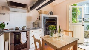 A kitchen with a built-in oven, a dining table with chairs, and a view of the garden through an open door. - 2 Bed in St. Ives (oc-3wd) (St Ives)
