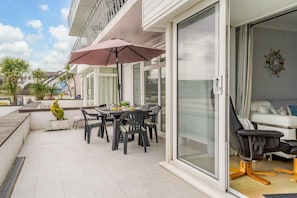 A modern outdoor patio with a table and chairs, a large umbrella, and a sliding glass door leading to a living area with a sofa and a coffee table. - 3 Bed in Saundersfoot (oc-pw230) (Saundersfoot)