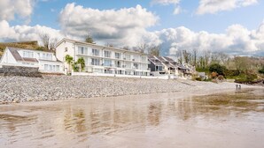 A beachfront hotel with multiple floors, a rocky shoreline, and a clear sky.