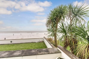 A beach view from a balcony with palm trees and a grassy area. - 3 Bed in Saundersfoot (oc-pw230) (Saundersfoot)