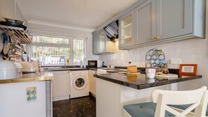 A compact kitchen with a washing machine, a microwave, and a dining area with a chair.