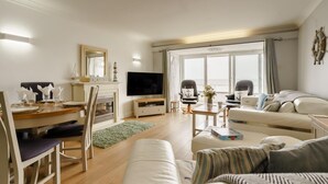 A modern living room with a fireplace, a TV, a dining area, and a large window with a view.