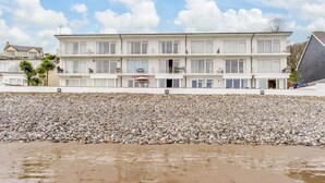 Un hotel frente a la playa con varios balcones, una playa de guijarros y cielo despejado.