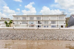 A beachfront hotel with multiple balconies, a pebble beach in front, and a clear sky. - 3 Bed in Saundersfoot (oc-pw230) (Saundersfoot)